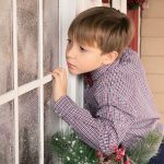 Boy Looking Into Window With Artificial Snow